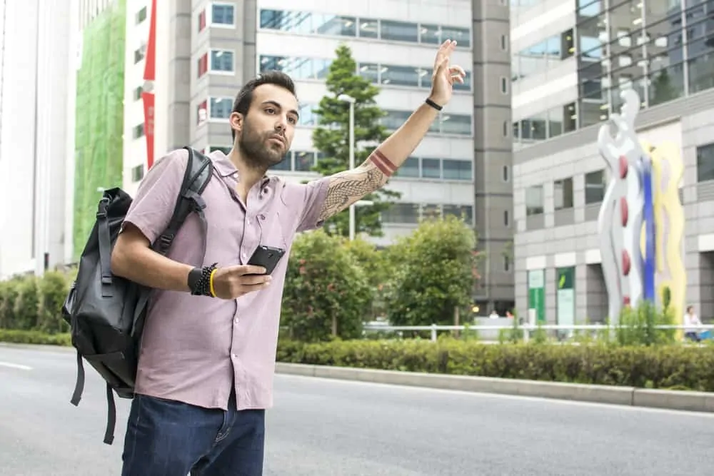 Man hailing and uber in a modern city on the side of the road.