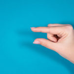 Closeup top view horizontal photography of female hand forming gesture Little bit. Empty space between two fingers of woman. Isolated on bright blue background.