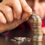 Man in a red and black flannel carefully stacking coins on a brown table