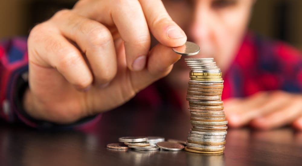 Man in a red and black flannel carefully stacking coins on a brown table