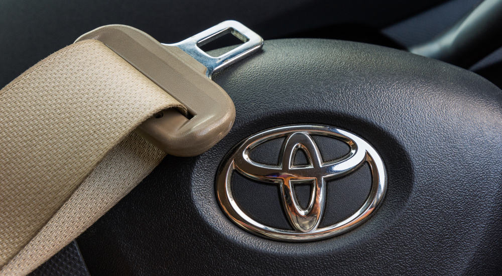 Brown seatbelt with silver buckle laid across black steering wheel with Toyota logo on it