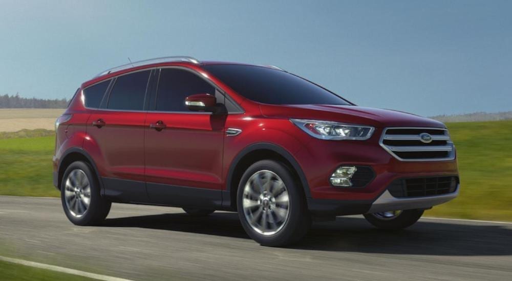 A red 2018 Ford Escape driving on a grassy road against a clear blue sky
