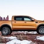 Profile of a gold 2019 Ford Ranger is on partly snowy ground in front of mountains.