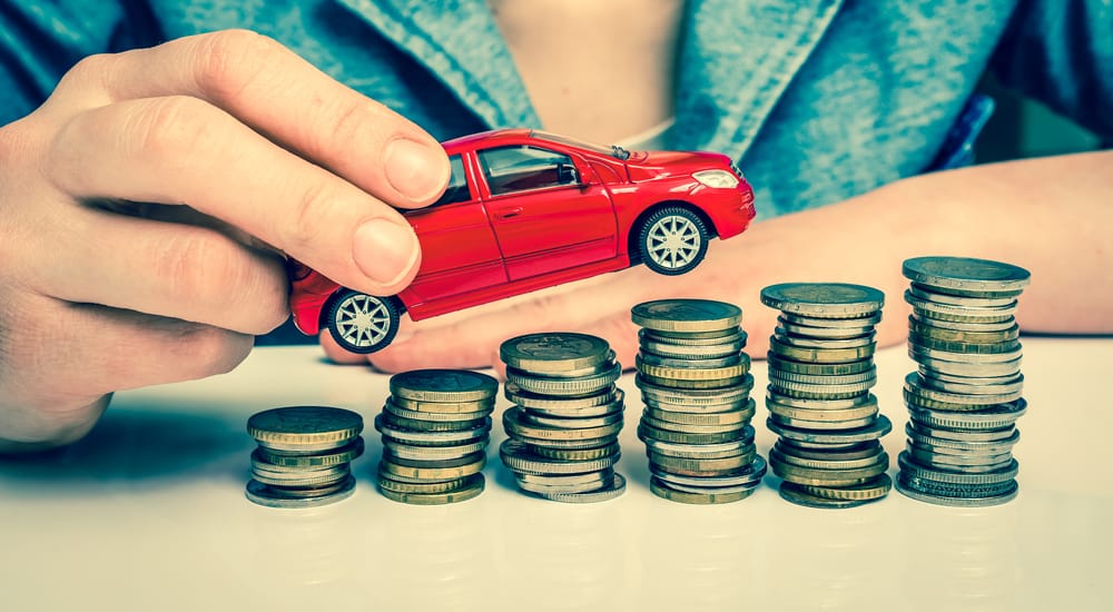Woman in a blue shirt holding a red toy car above six increasingly taller stacks of coins