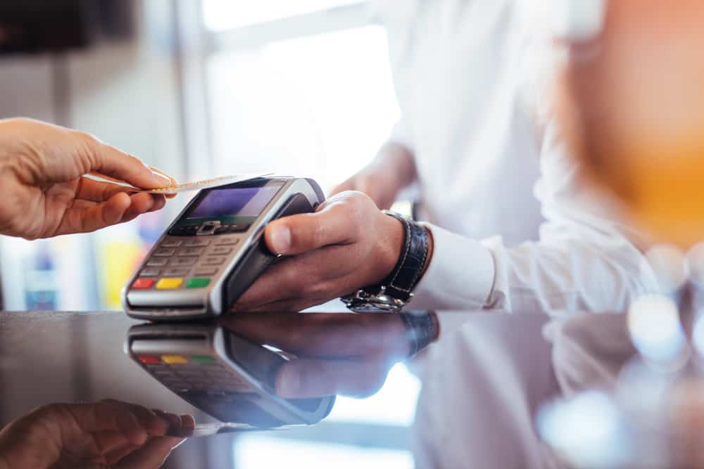 Hand of customer paying with contactless credit card with NFC technology. Bartender with a credit card reader machine at bar counter with female holding credit card. Focus on hands.