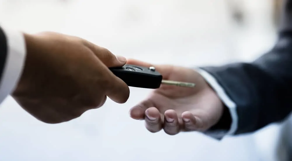 Up close of a man in a suit handing a car key to another man in a suit