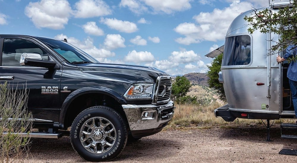 The front of a black Ram 2500HD from your local RAM Dealership next to an Airstream camper against a cloudy and blue desert sky