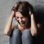 Woman screaming while sitting against wall after being frustrated by her car buying experience