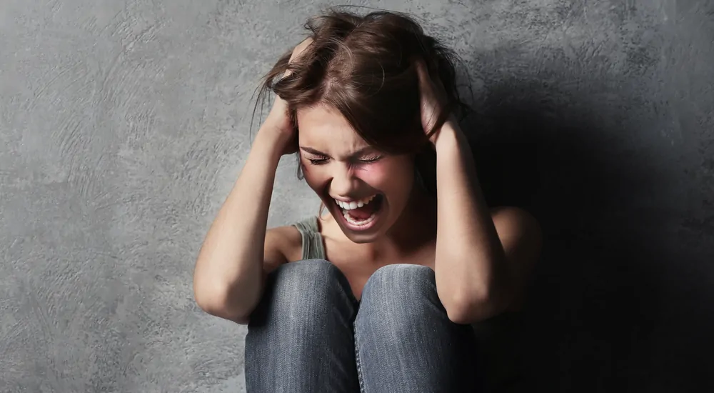 Woman screaming while sitting against wall after being frustrated by her car buying experience