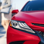 Closeup of red 2019 Toyota Camry headlight. Man and woman out of focus in back