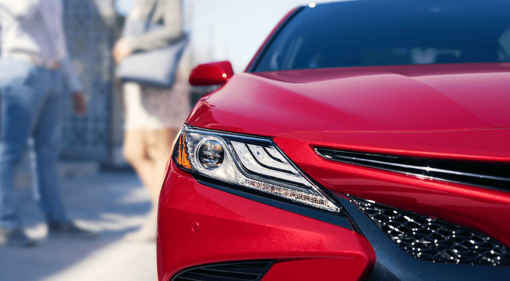 Closeup of red 2019 Toyota Camry headlight. Man and woman out of focus in back