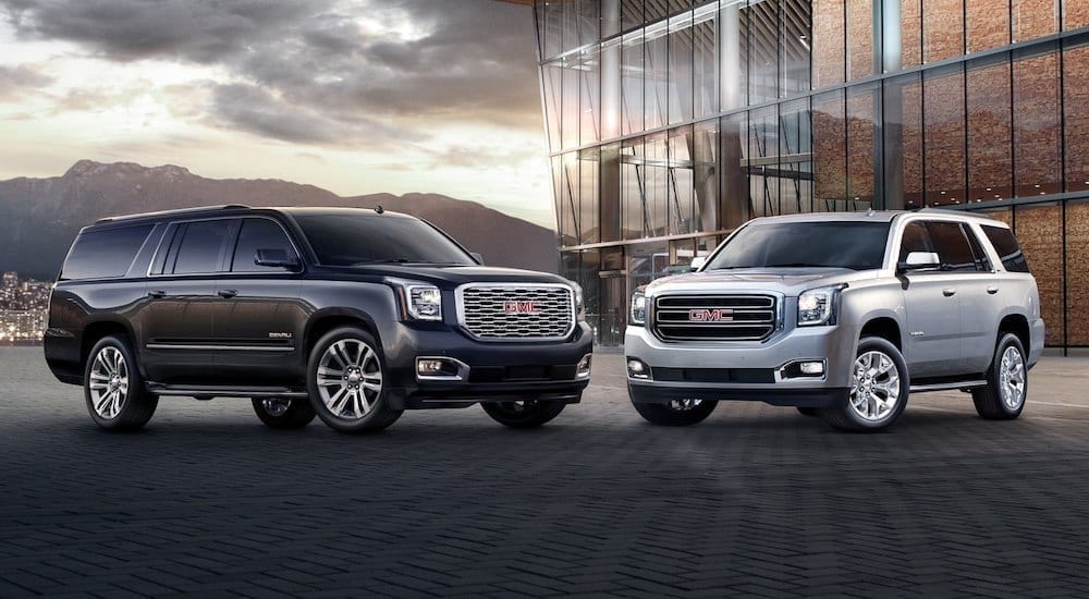 Silver 2019 GMC Yukon and Black Yukon Denali in front of glass building