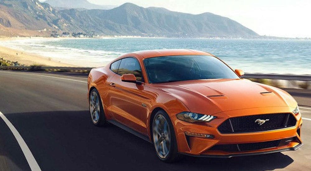 An orange Ford Mustang drives down a costal highway