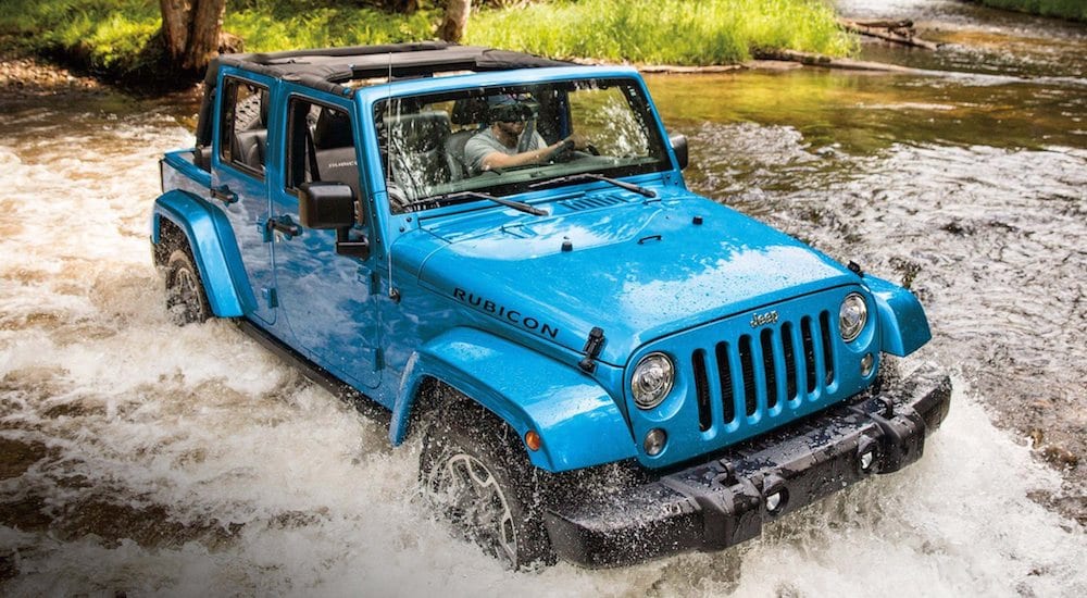 A Blue 2018 Jeep JK crosses a deep river