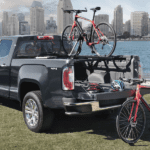 Black 2019 GMC Canyon with 2 bikes at park in front of river and city skyline