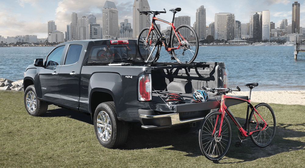 Black 2019 GMC Canyon with 2 bikes at park in front of river and city skyline