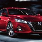 Red 2019 Nissan Altima driving at nigh with out of focus background
