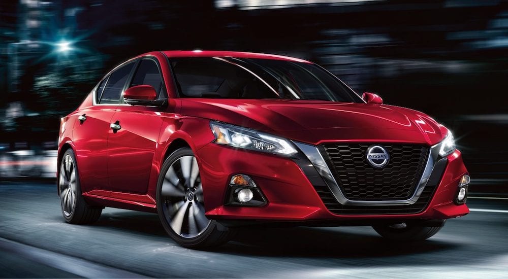 Red 2019 Nissan Altima driving at nigh with out of focus background