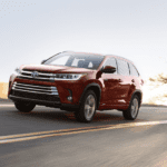 A red 2019 Toyota Highlander drives a empty sunny highway