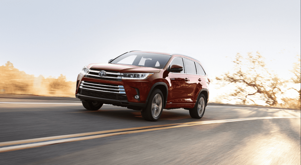 A red 2019 Toyota Highlander drives a empty sunny highway