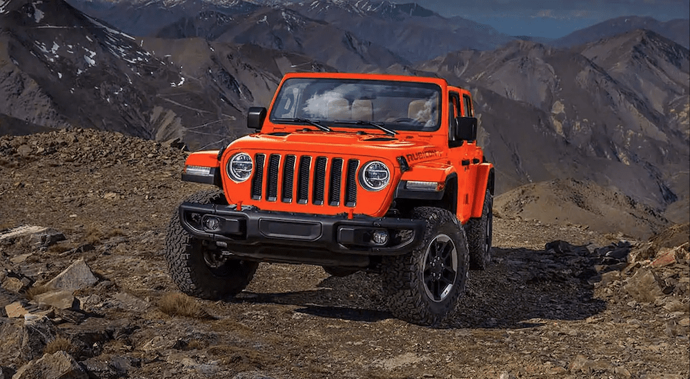 A bright orange 2019 Jeep Wrangler climbs a rocky mountain
