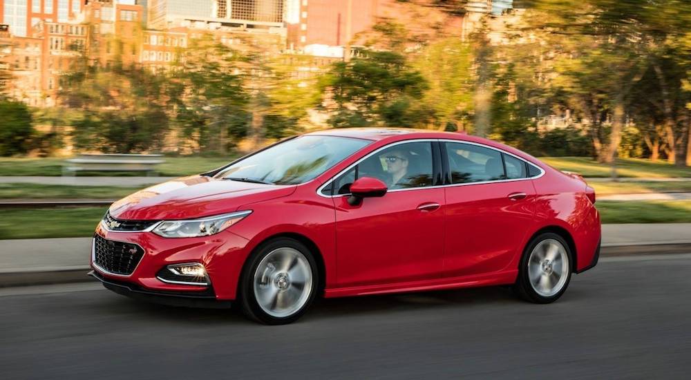 A red used Chevy Cruze driving on a quiet tree lined street