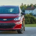 A red 2019 Chevrolet Bolt EV in front of a large white house in the country