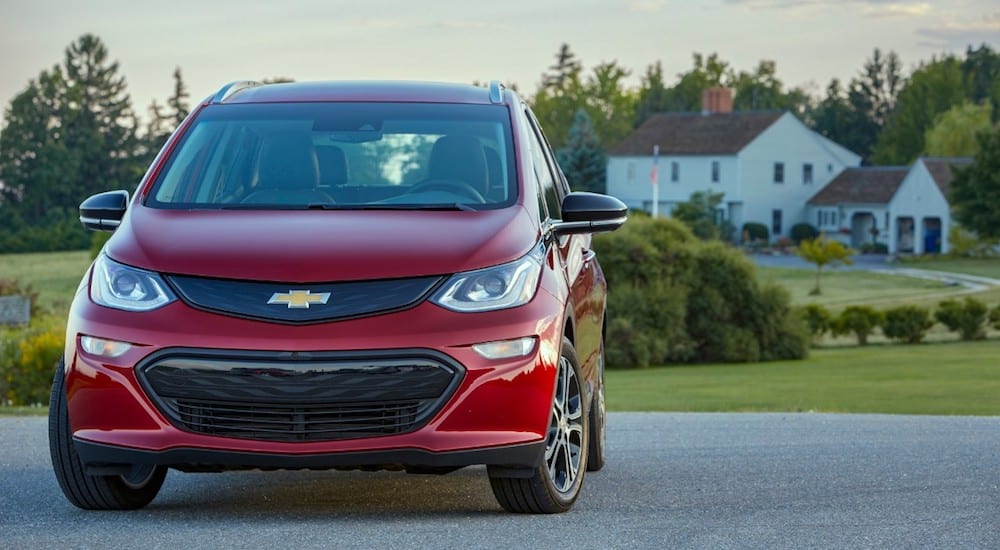 A red 2019 Chevrolet Bolt EV in front of a large white house in the country