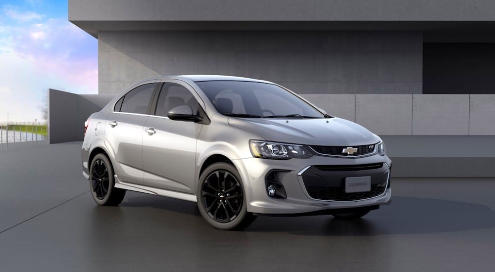 A silver 2019 Chevy Sonic sedan parked in front of a concrete building