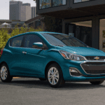 A blue 2019 Chevy Spark parked in front a metal building with bamboo