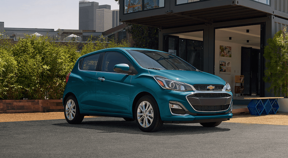 A blue 2019 Chevy Spark parked in front a metal building with bamboo