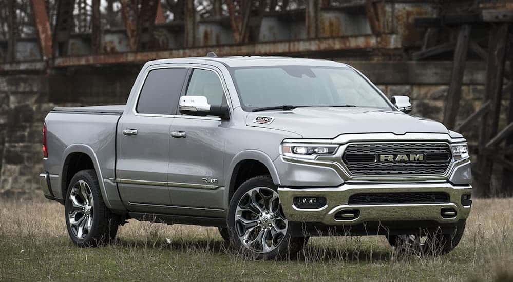A silver 2020 Ram 1500 is parked in a grassy field with a rusty bridge in the background.
