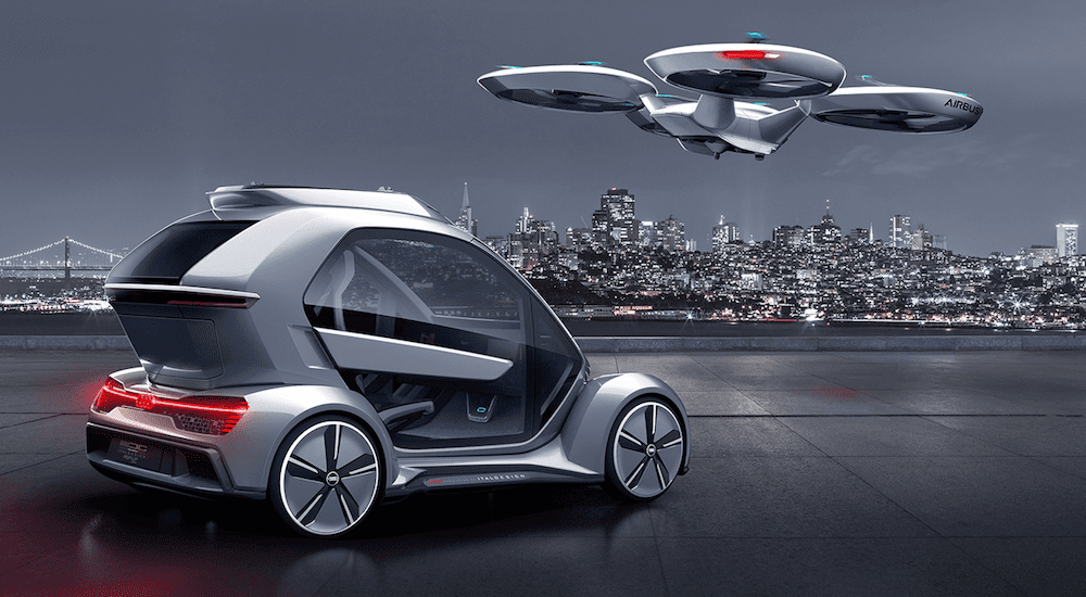 A silver Audi Pop.up.Next concept car and drone with NYC in the back at night