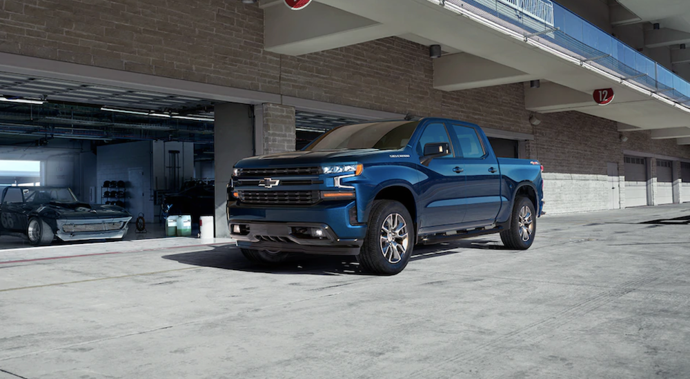 A blue 2019 Chevy Silverado is parked in front of an open garage door with a race car in the bay.
