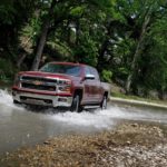 A red 2015 Chevy Silverado driving through a river