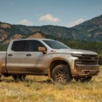 A light colored 2019 Chevy Silverado 1500 is muddy in a field.