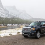 A black 2019 GMC Sierra 2500HD Denali is on the side of the road with snowy mountains behind it.