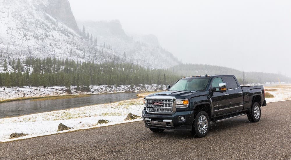 A black 2019 GMC Sierra 2500HD Denali is on the side of the road with snowy mountains behind it.
