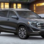 A grey 2019 GMC Terrain is parked in the driveway of a modern house.