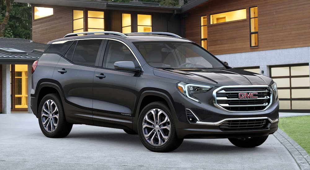 A grey 2019 GMC Terrain is parked in the driveway of a modern house.