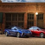 A red and a blue 2019 Toyota Mirai are parked out of a brick building.