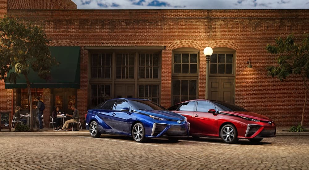 A red and a blue 2019 Toyota Mirai are parked out of a brick building.