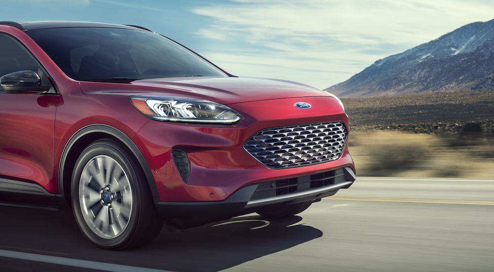 A red 2020 Ford Escape Hybrid is driving with mountains in the distance.