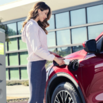 A woman is charging a red 2020 Ford Escape Plug-in. In current auto news, Ford plans to have more electric vehicles.