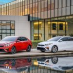 A red and a white 2019 Kia Forte are parked outside of a dealership. Find yours by searching 'Kia dealership near me'.