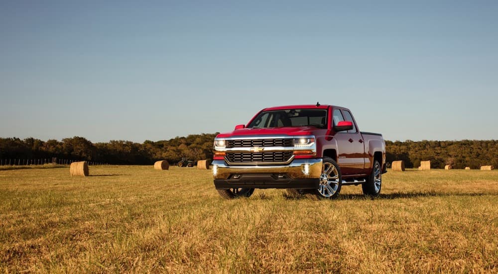 A red 2016 Chevy Silverado 1500 is parked in a hay field.