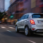 A white 2019 Chevy Trax is driving through the city at dusk.