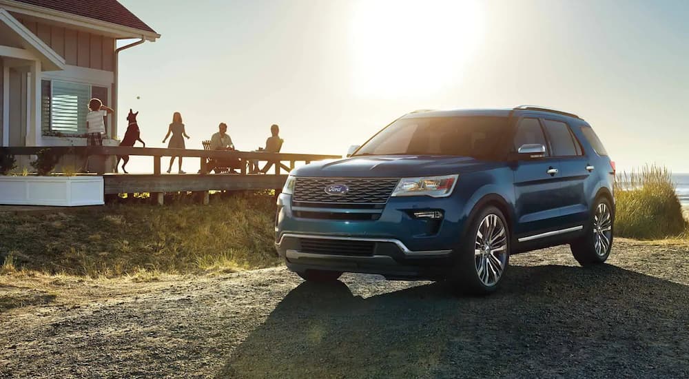 a 2019 blue Ford Explorer is parked outside a beach house while the family is on the deck.