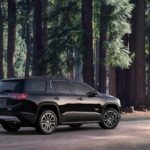 A black 2019 GMC Acadia is parked in front of tall trees in the forest.