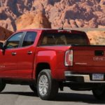 A red 2019 GMC Canyon is parked in front of red rocks.